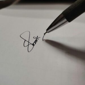Macro shot of a pen writing a signature on white paper, emphasizing precision.