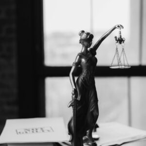 Grayscale photo of Lady Justice statue beside legal documents on a wooden table.